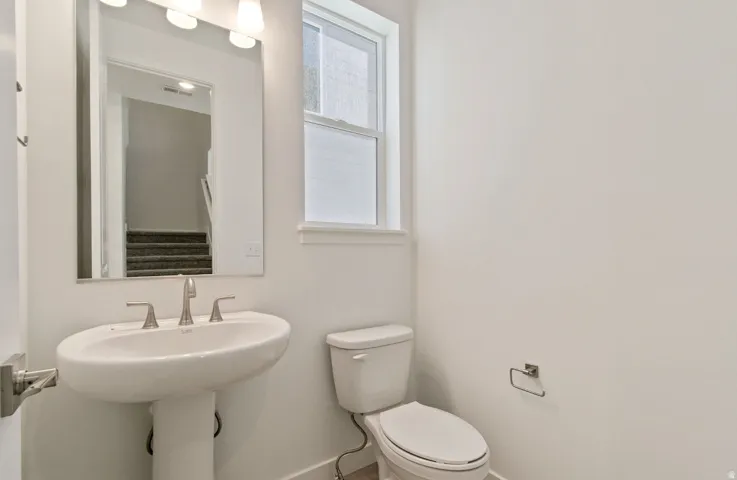 Bathroom featuring a pedestal sink, brushed nickel faucet, wall-mounted mirror, and a window with blinds