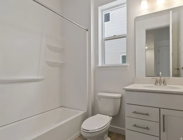 Bathroom featuring a tub/shower combination with integrated shelving, a single-sink vanity with white cabinetry and a light-toned countertop, and an elongated toilet