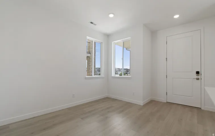 Bright room featuring two windows, wood-finish flooring, white trim, recessed lighting, and a paneled door with contemporary hardware