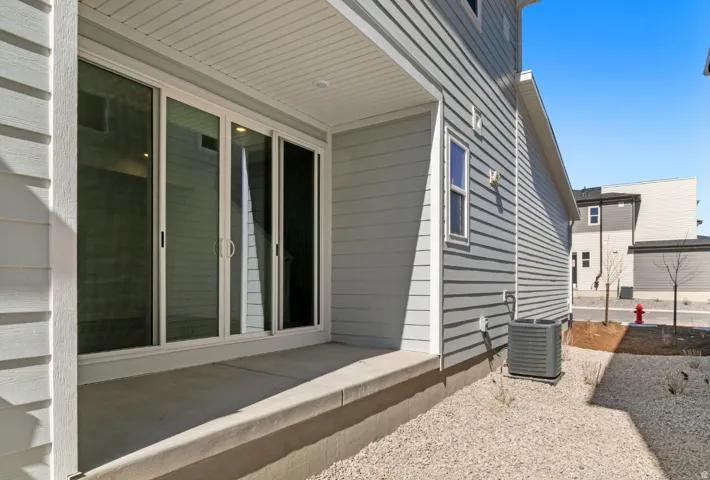 Concrete patio with covered overhead, featuring a sliding glass door system, light gray horizontal siding, and a gravel hardscape