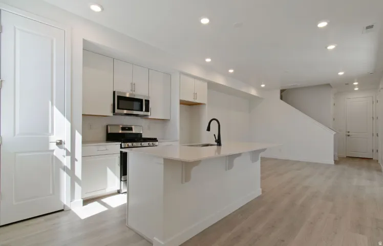 Modern kitchen featuring a central island with an integrated sink, quartz countertops, stainless steel appliances, and white shaker cabinetry