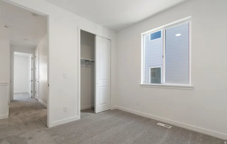 Carpeted room featuring a large window, white trim, and a bi-fold closet with shelving and hanging rod