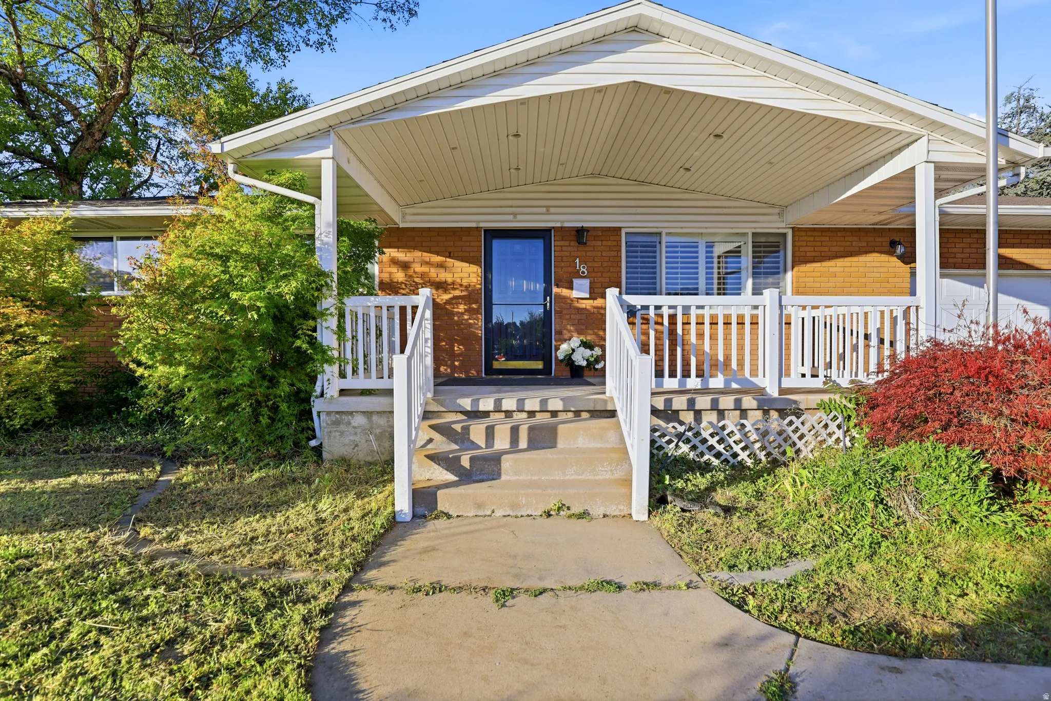 Brick exterior with a covered front porch, concrete entry path, white railings, and mature landscaping