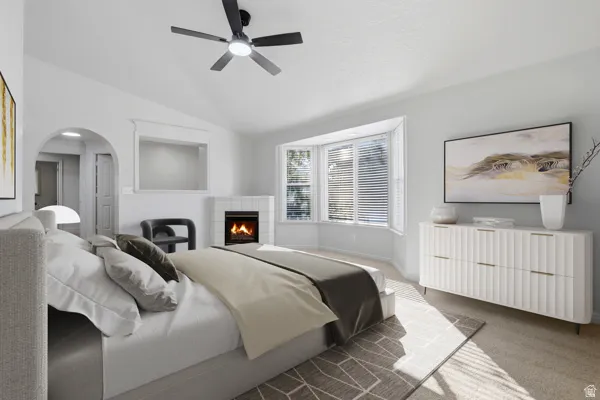 Bedroom featuring a bay window, recessed fireplace with tile surround, vaulted ceiling, and an arched doorway