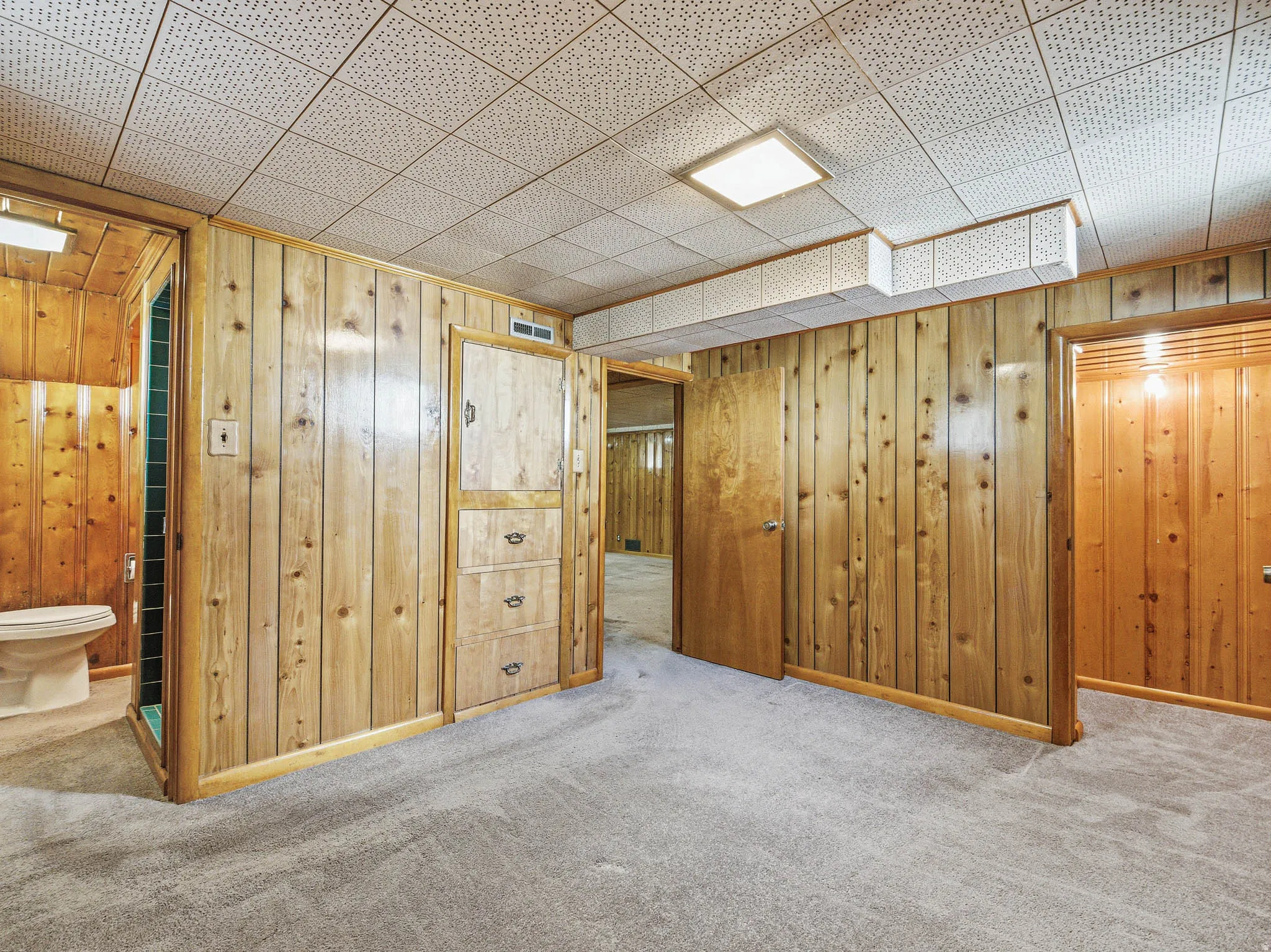 Carpeted room featuring extensive wood paneling and a drop ceiling with recessed lighting