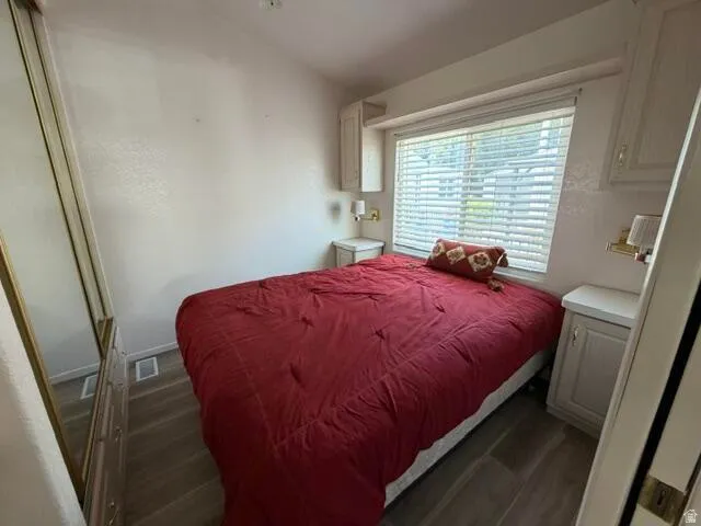 Bedroom featuring wood-finish flooring, a window with blinds, and built-in cabinetry