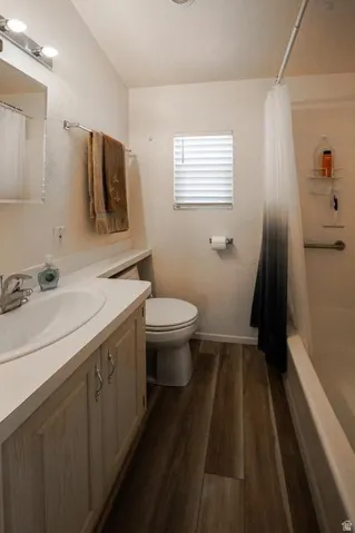Bathroom featuring wood-finish flooring, a white vanity with integrated sink, a built-in bathtub, a window with blinds, and overhead lighting