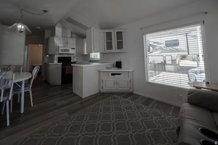 Open-concept kitchen and living area featuring wood-finish flooring, white cabinetry, a built-in oven, and a large window with horizontal blinds