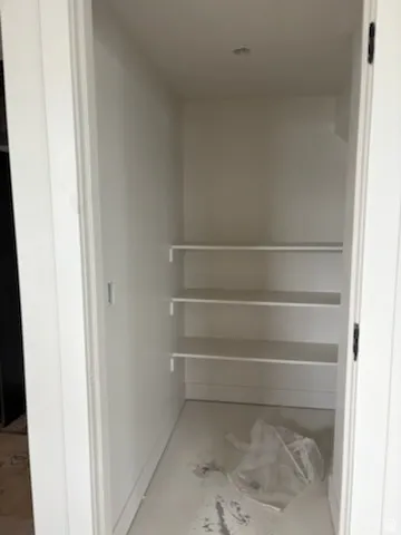 Closet space featuring three white shelving units, white walls, and a white baseboardit is a pantry area for kitchen in basement.
