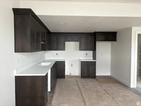 Basement kitchen, featuring dark wood cabinetry with crown molding, white countertops, and an undermount sink
