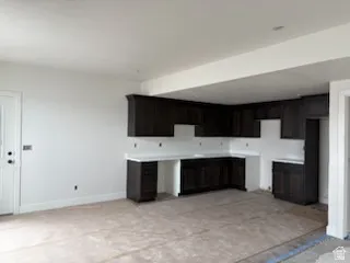 Kitchenette area featuring dark wood-finish cabinetry, white countertops, and a white interior door