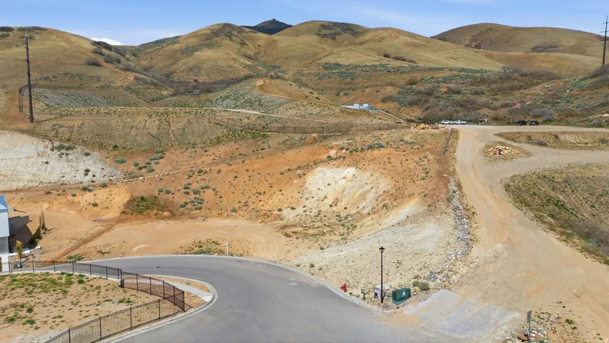 Sloping terrain with natural vegetation, featuring a paved cul-de-sac and a partial perimeter fence