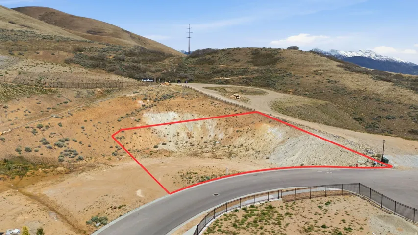 Unimproved lot with a defined boundary line, featuring a paved road frontage and surrounding natural terrain