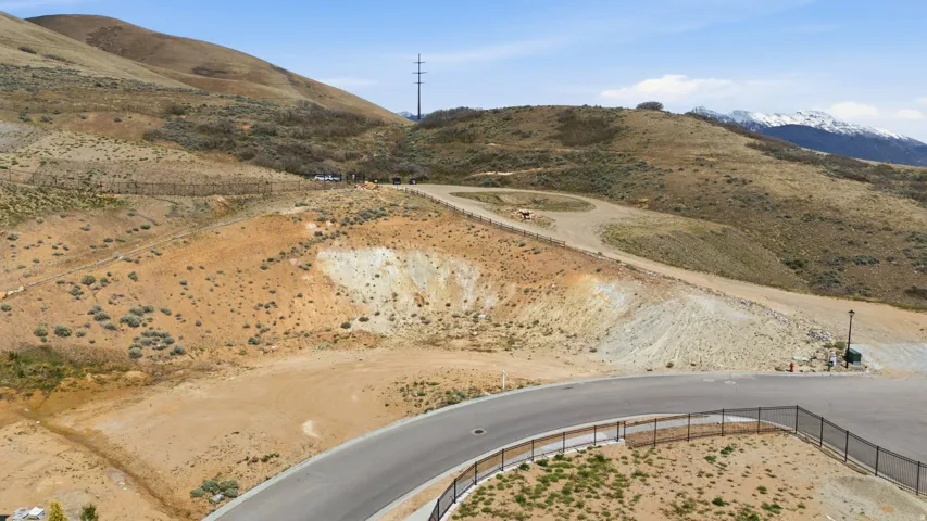 Expansive undeveloped land featuring a paved road, partial fencing, varied terrain, and distant snow-capped mountains