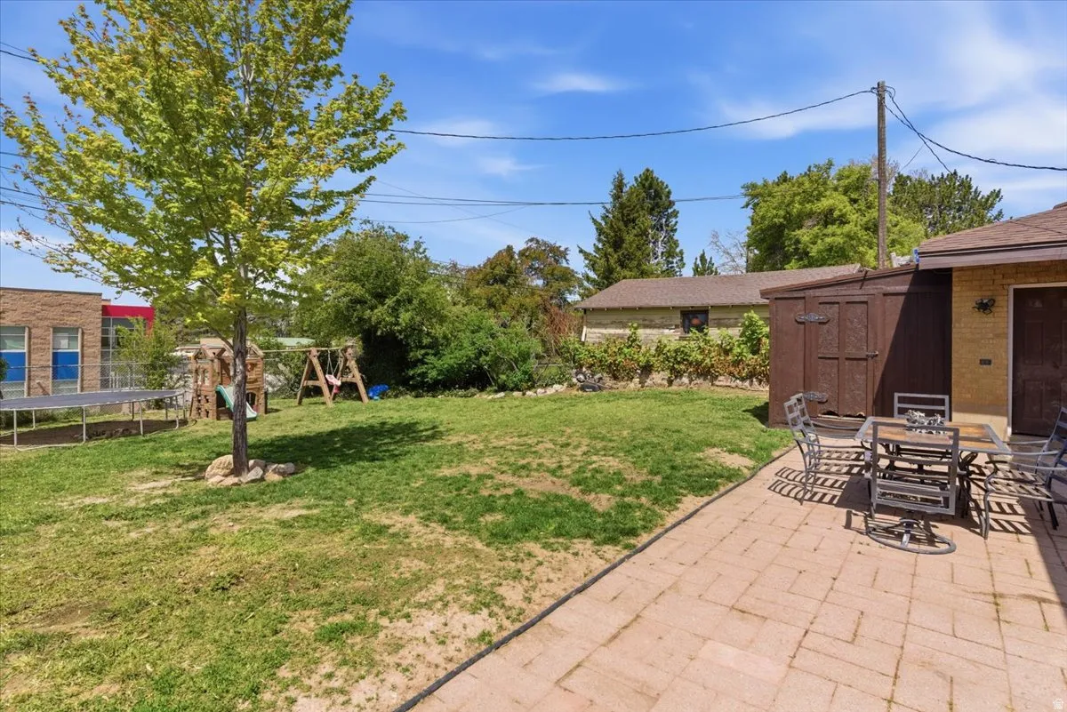 Expansive backyard featuring a paver patio, a freestanding storage shed, and mature trees