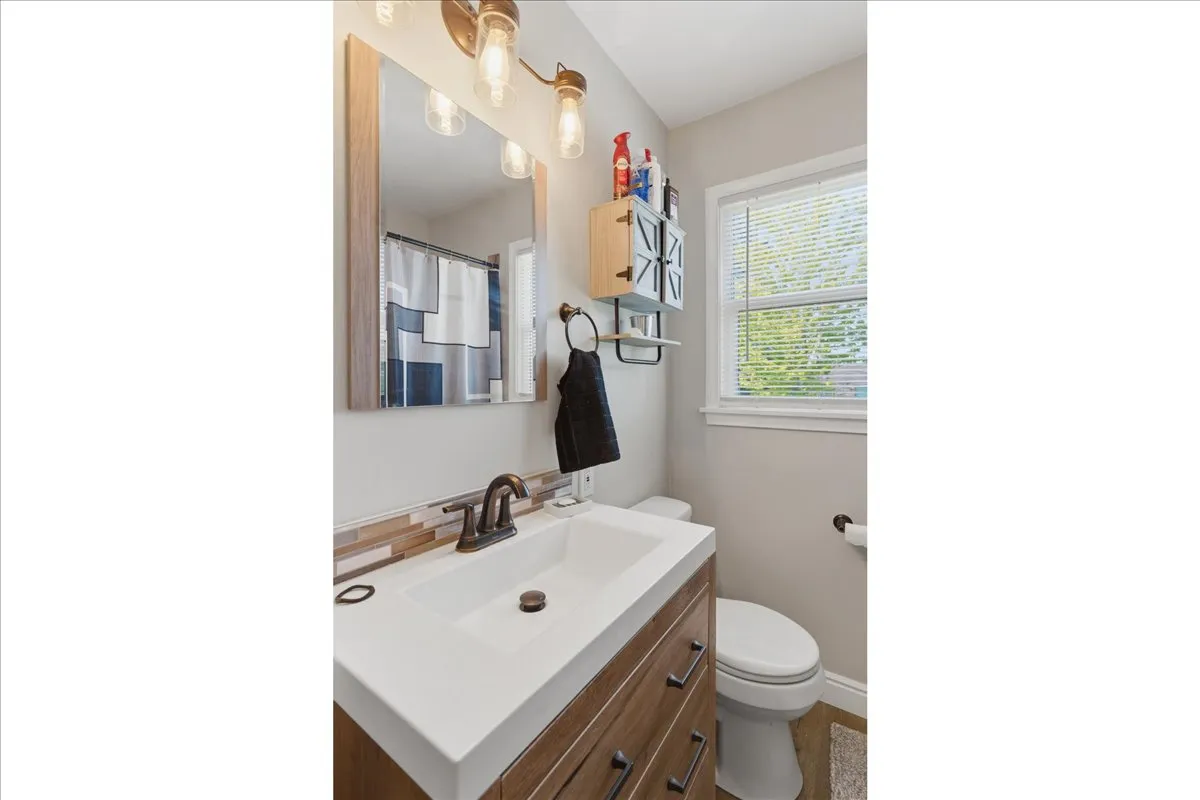 Bathroom featuring a wood-finish vanity with a white rectangular sink, bronze faucet, and a multi-toned tile backsplash