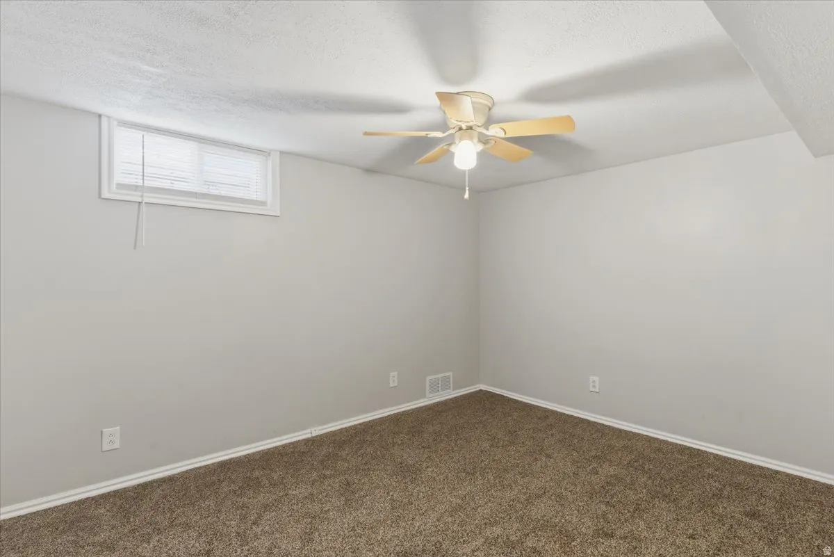 Room featuring neutral tone walls, brown carpeting, and a ceiling fan with light fixture