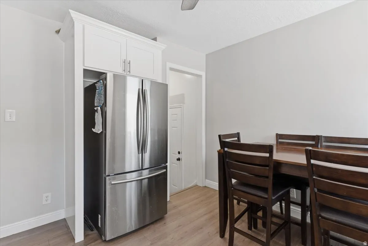 Stainless steel refrigerator integrated with custom white upper cabinetry, wood-finish flooring, and a dark wood dining set