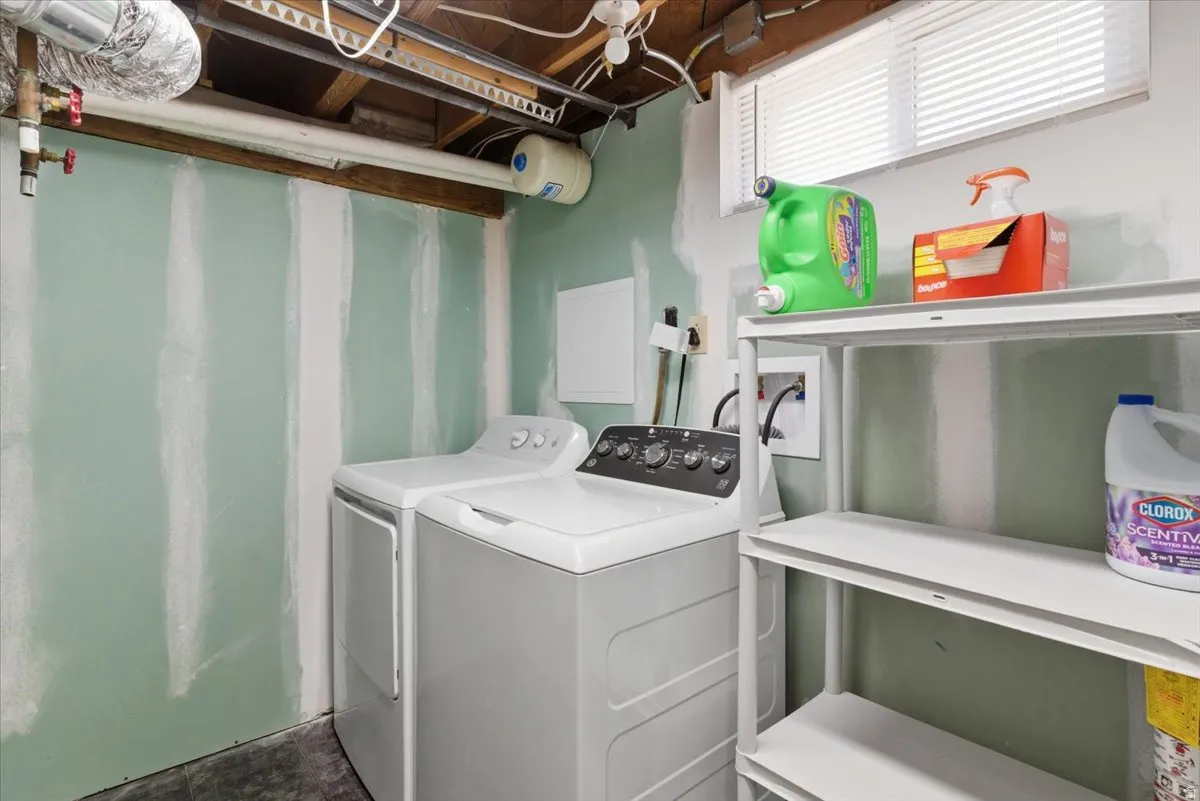 Laundry area featuring an exposed ceiling, light green drywall, a window with blinds, and white shelving units