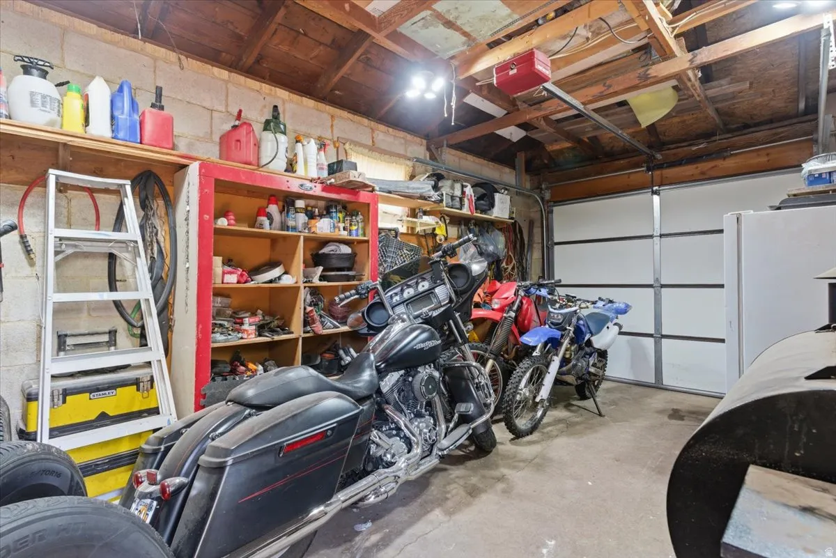 Garage interior featuring a sectional garage door, exposed wood rafters, concrete block walls, and built-in shelving