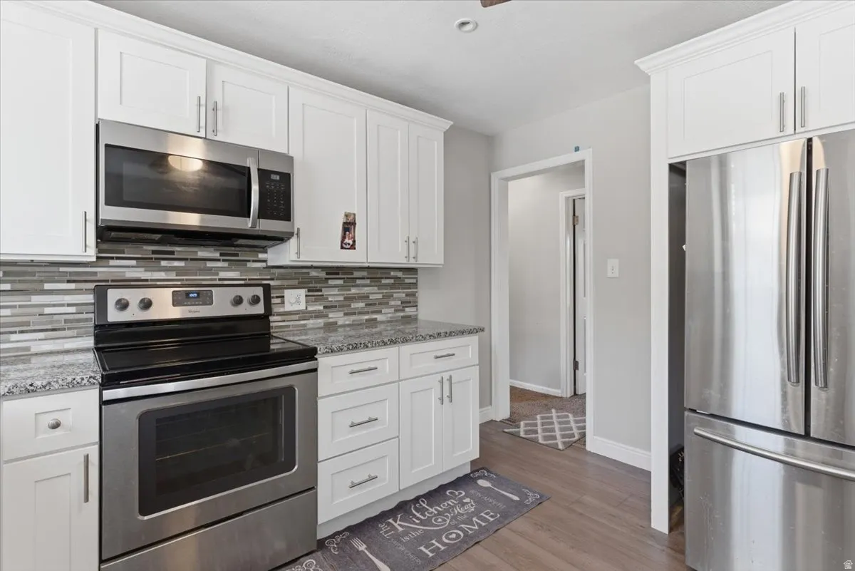 Contemporary kitchen featuring white shaker cabinetry, stainless steel appliances, granite-style countertops, mosaic tile backsplash, and wood-finish flooring