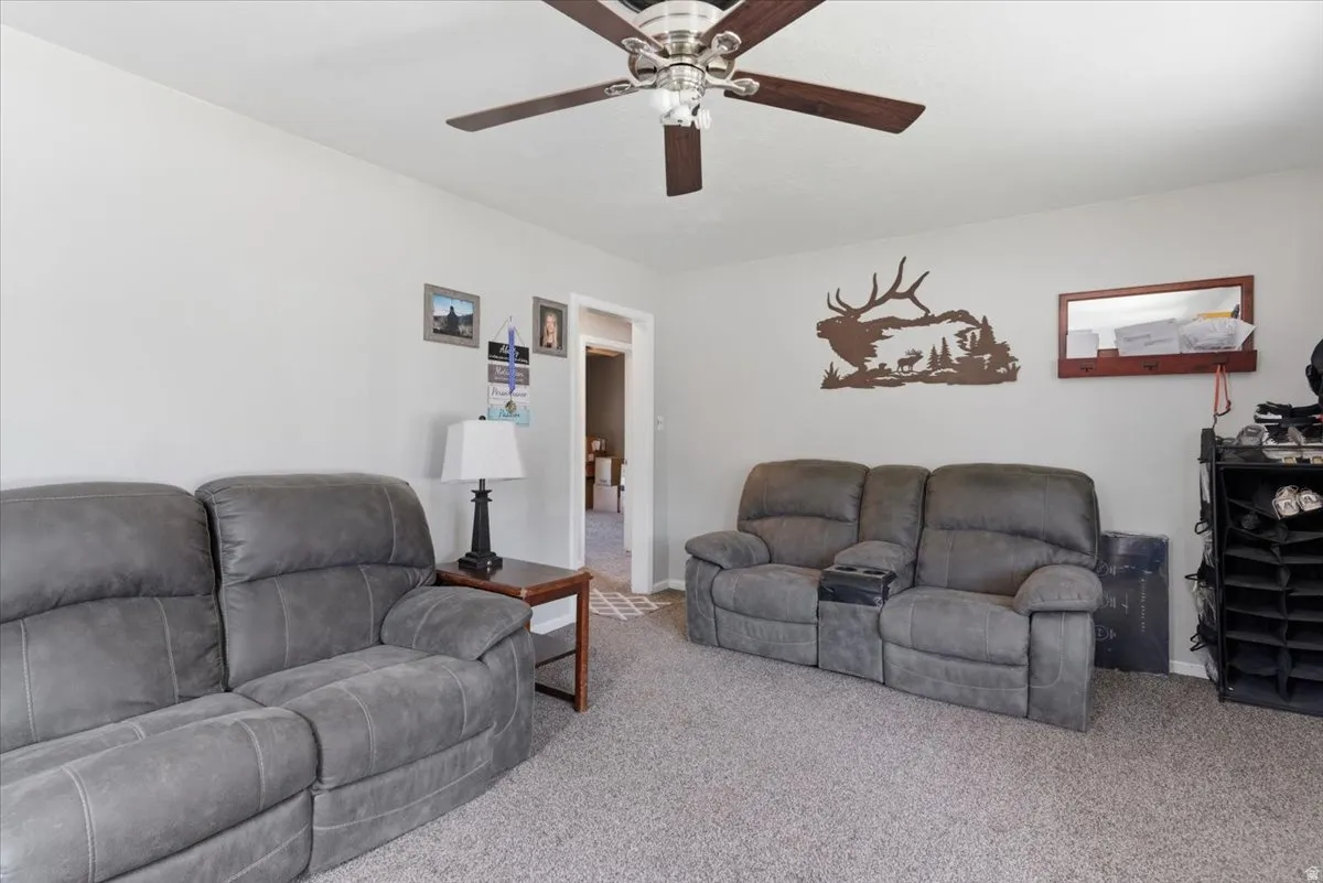 Living area featuring carpet flooring, light-toned walls, and a ceiling fan with wood-finish blades