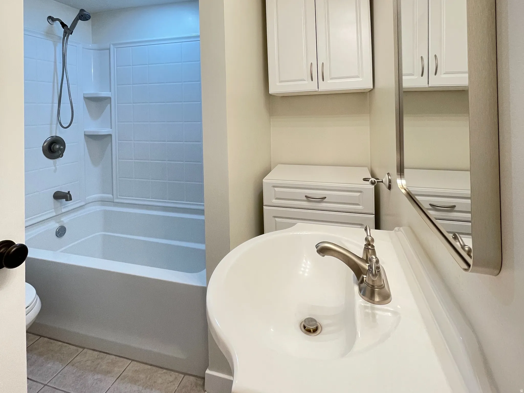 Bathroom featuring a white bathtub with, brushed nickel fixtures, a ceramic vanity sink with a brushed nickel faucet, a large wall mirror, and white cabinetry. Behind the door is access to the furnace.