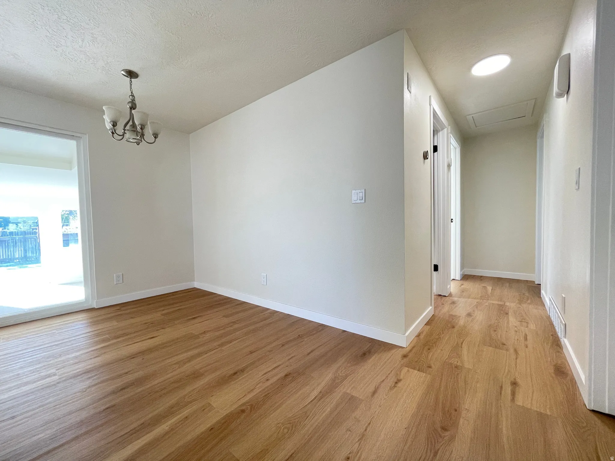 Bright interior space featuring wood-finish flooring, a contemporary chandelier, and a sliding glass door