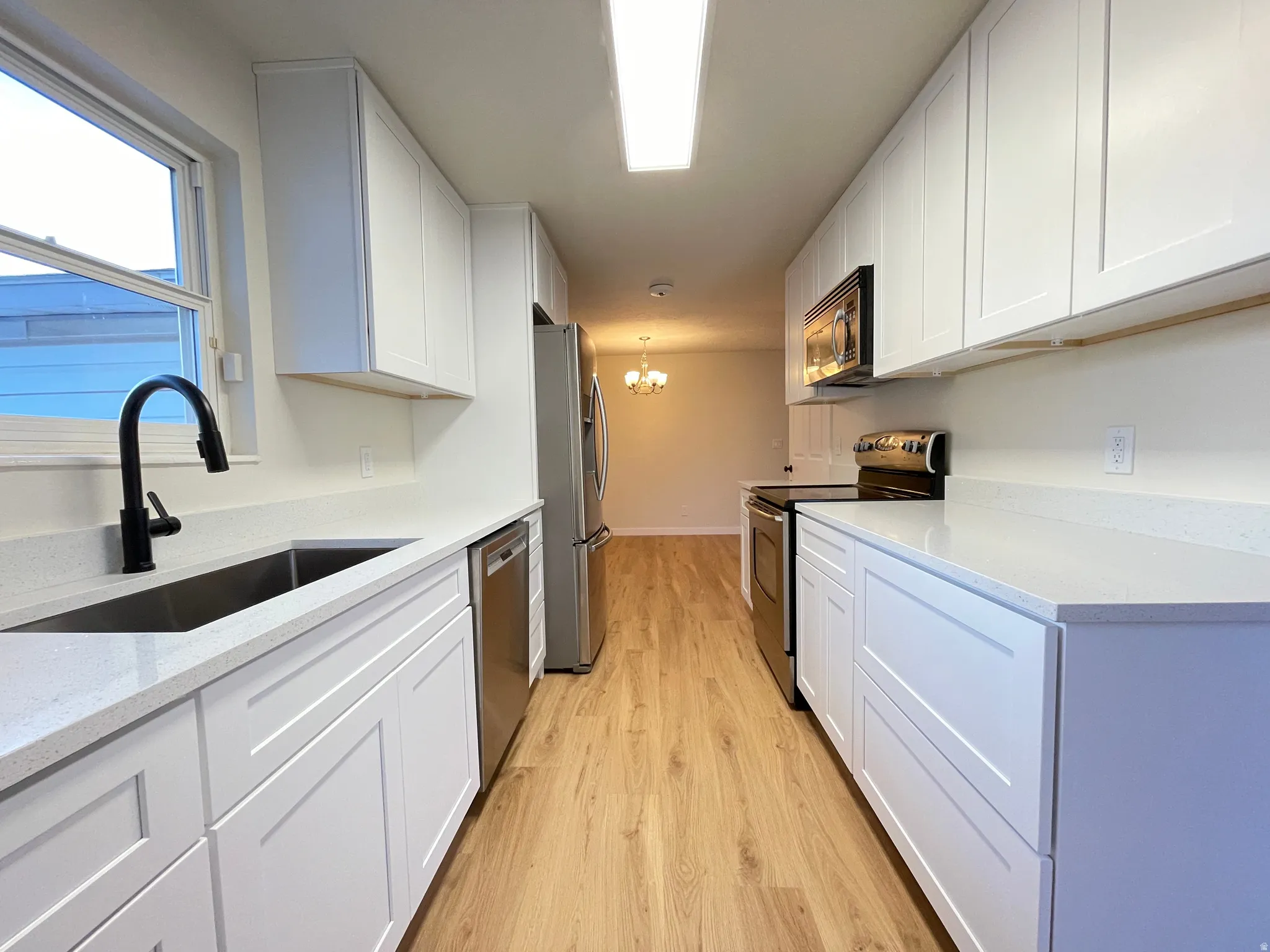 Galley kitchen featuring white shaker cabinetry, light-toned wood-finish flooring, and white countertops. Black cabinet handles soon to come!