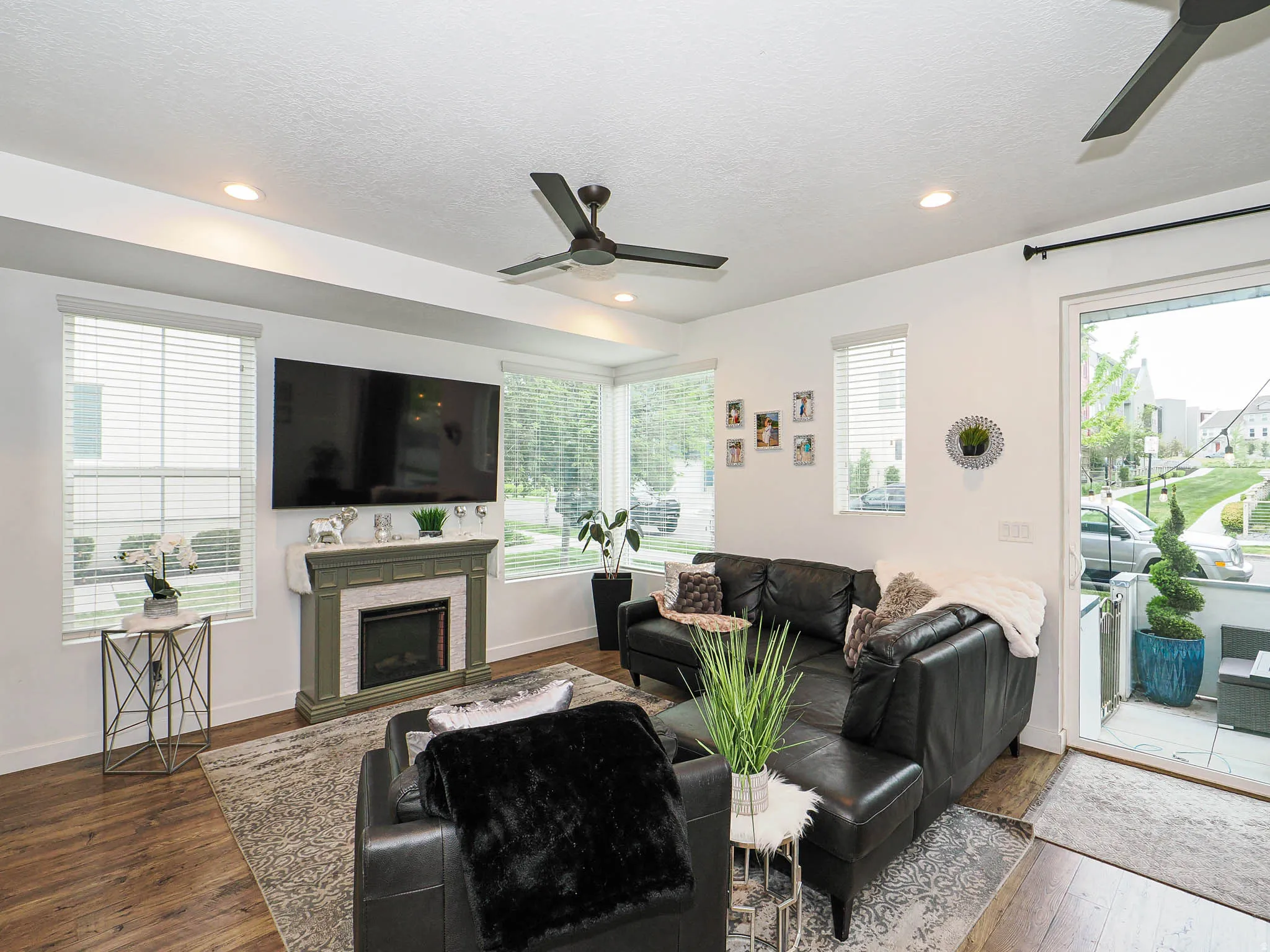 Living room featuring wood-finish flooring, a decorative fireplace with a mantel, multiple windows with blinds, a ceiling fan, and recessed lighting