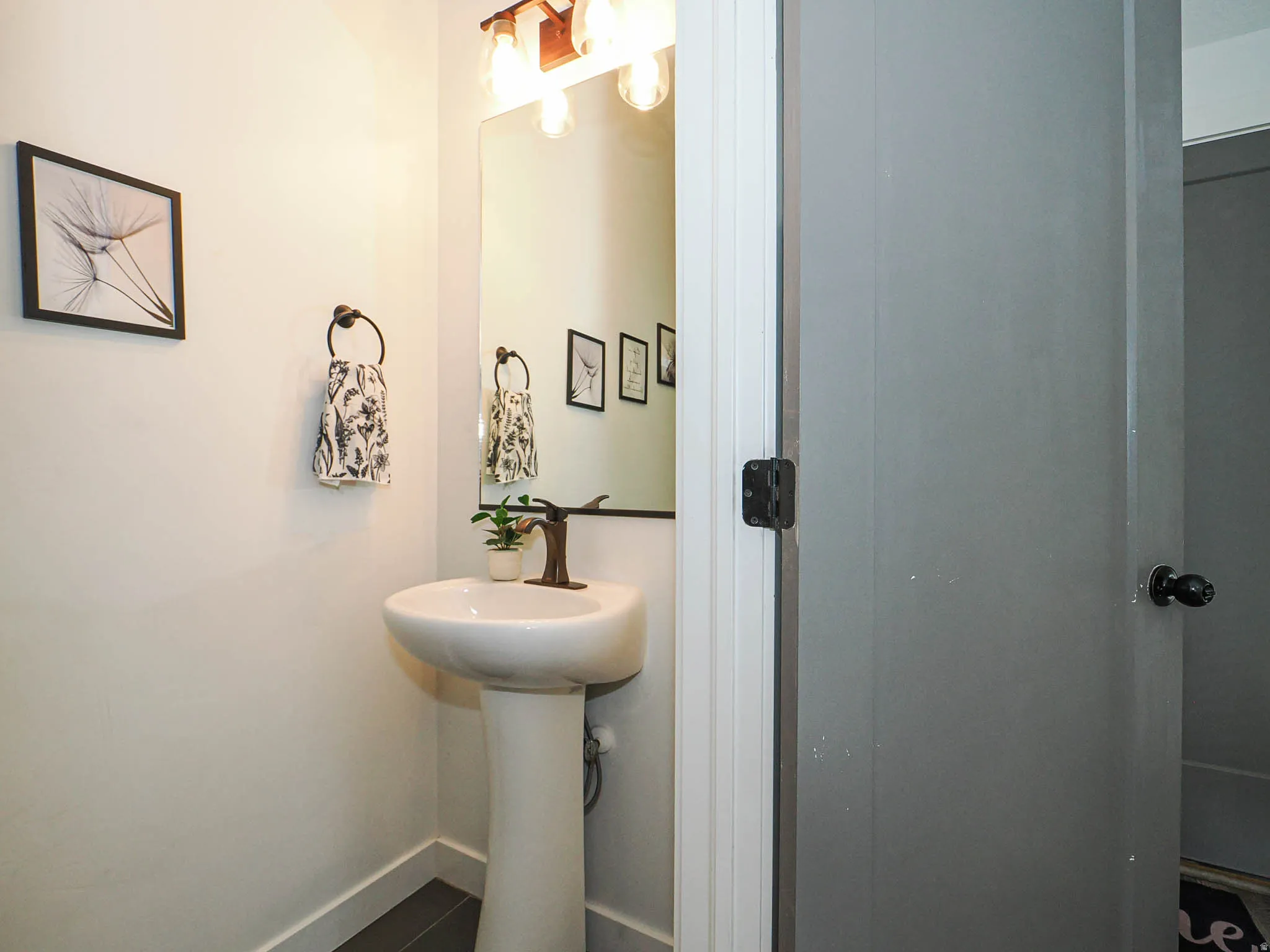 Pedestal sink with a bronze-finish faucet, mirror, and an overhead vanity light fixture