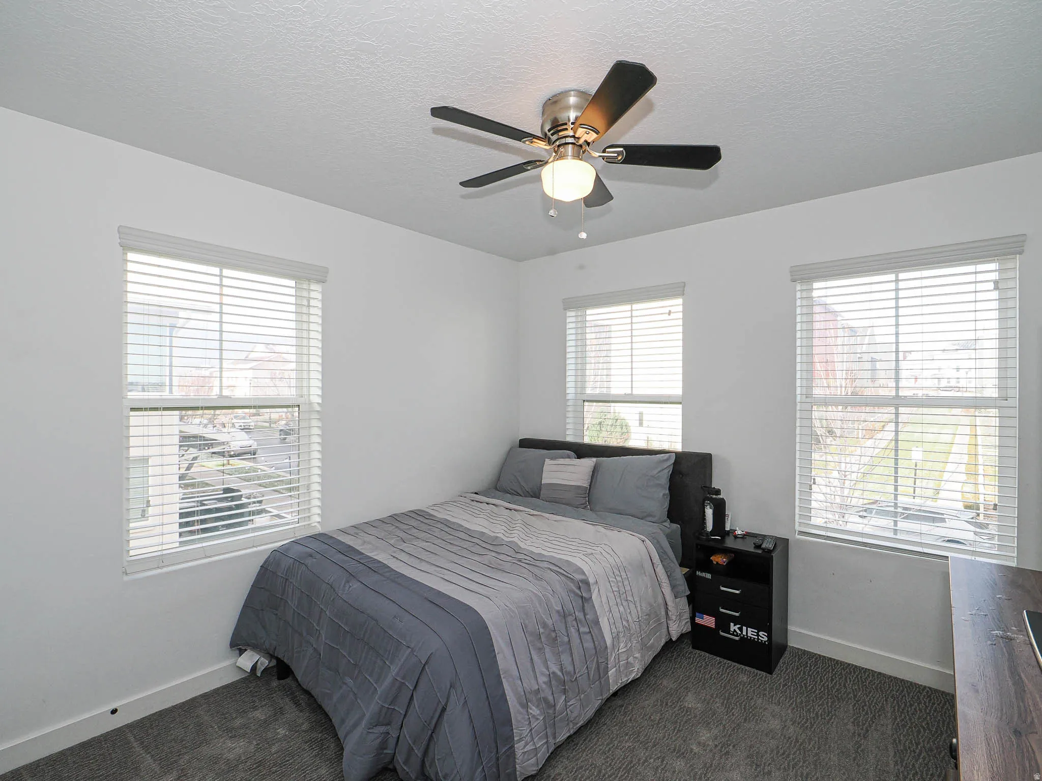 Bedroom with a textured ceiling, dark colored carpet, multiple windows, and a ceiling fan