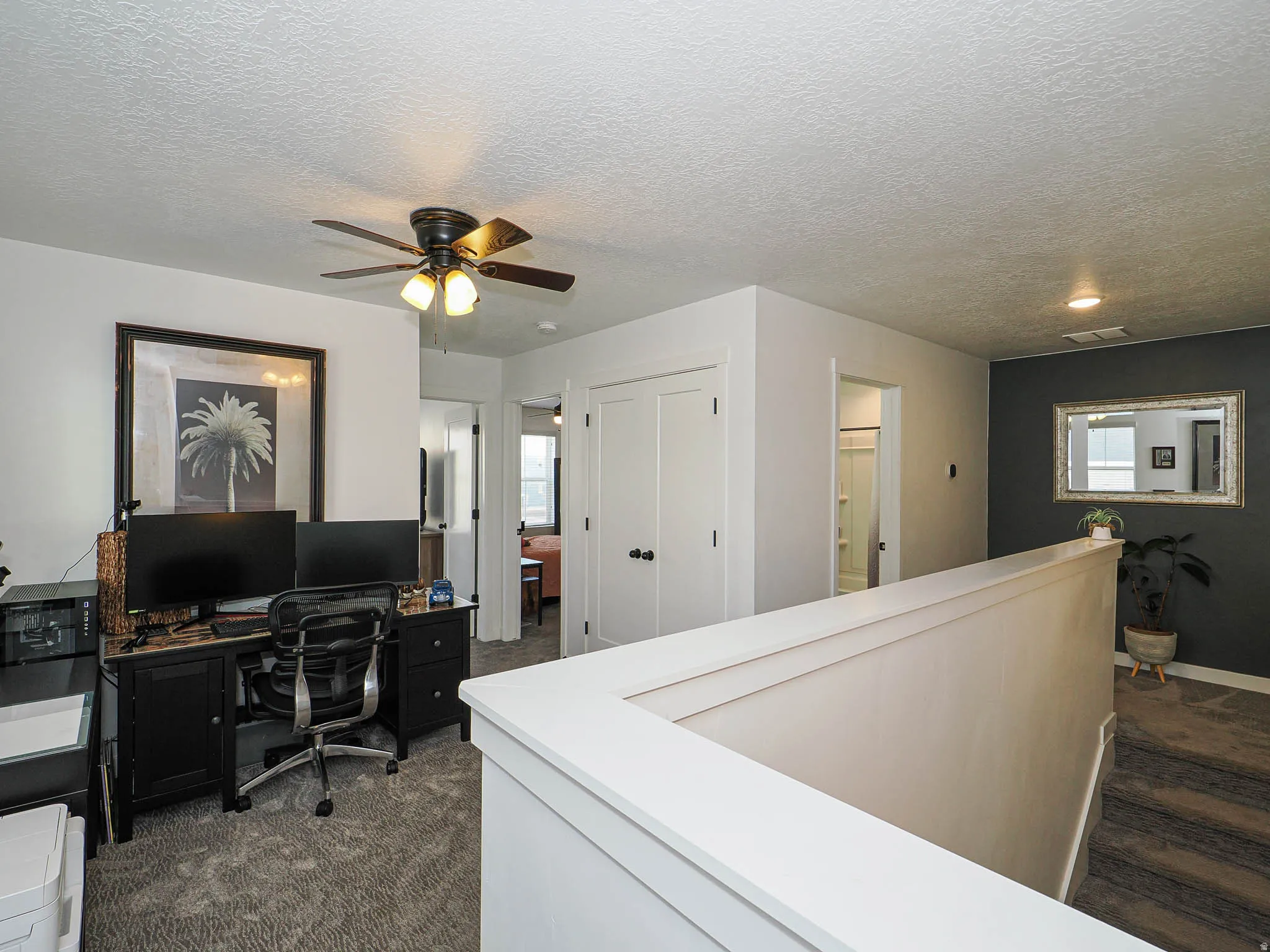 Office area with a textured ceiling, dark colored carpet, and a ceiling fan