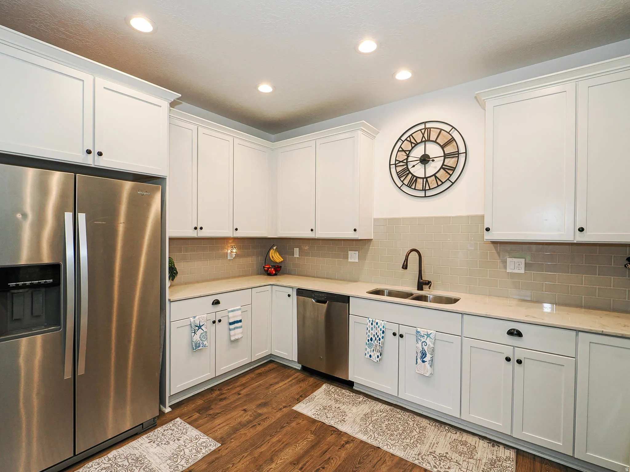 Kitchen featuring white shaker-style cabinetry, stainless steel appliances, light-colored countertops, a subway tile backsplash, and wood-finish flooring