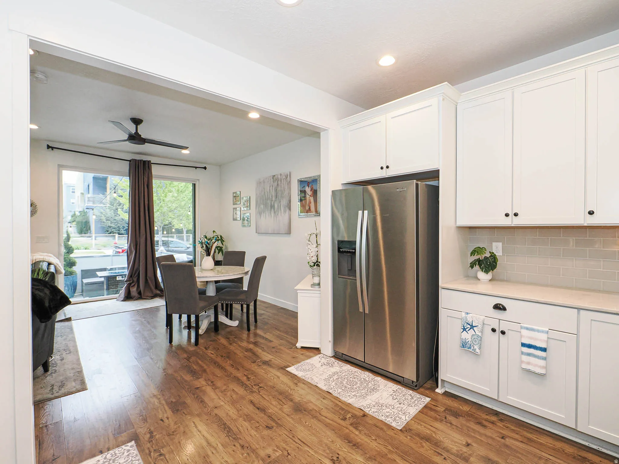 Open-concept living space featuring wood-finish flooring, a contemporary ceiling fan, and a kitchen with white cabinetry and a subway tile backsplash