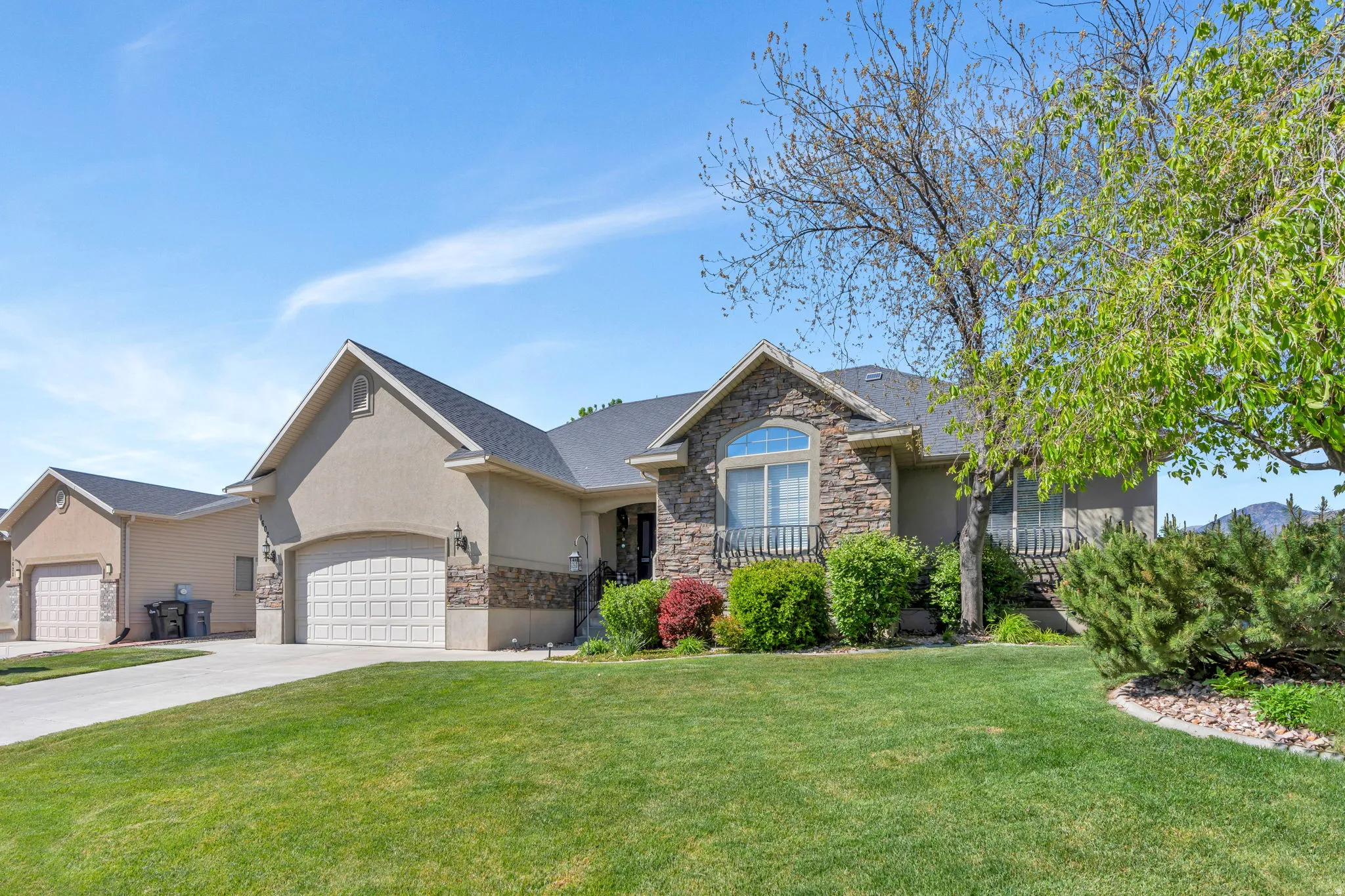 Single story home with stone siding, a front yard, stucco siding, concrete driveway, and a garage