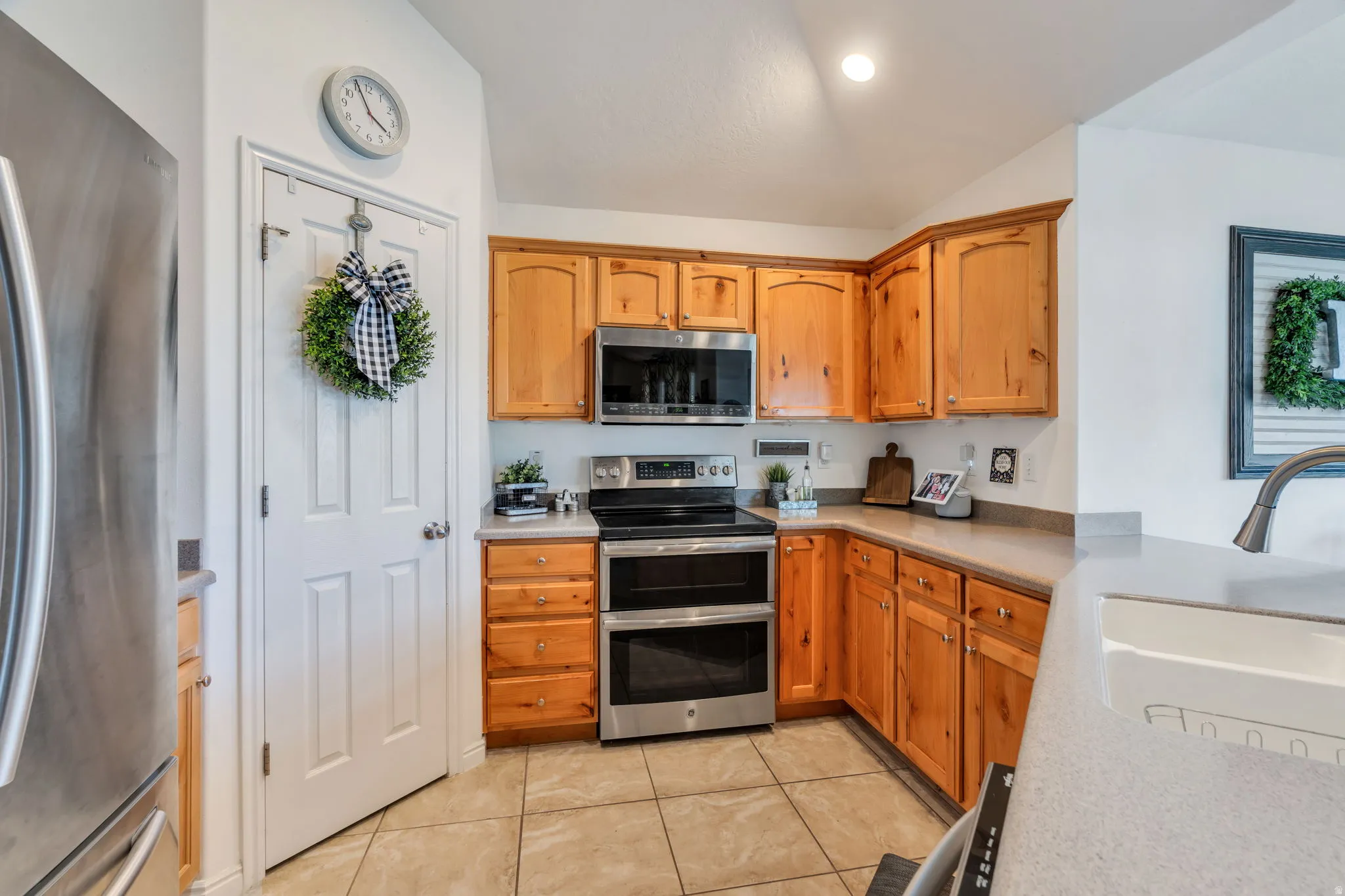 Kitchen featuring stainless steel appliances, vaulted ceiling, light tile patterned flooring, and wood finish cabinets