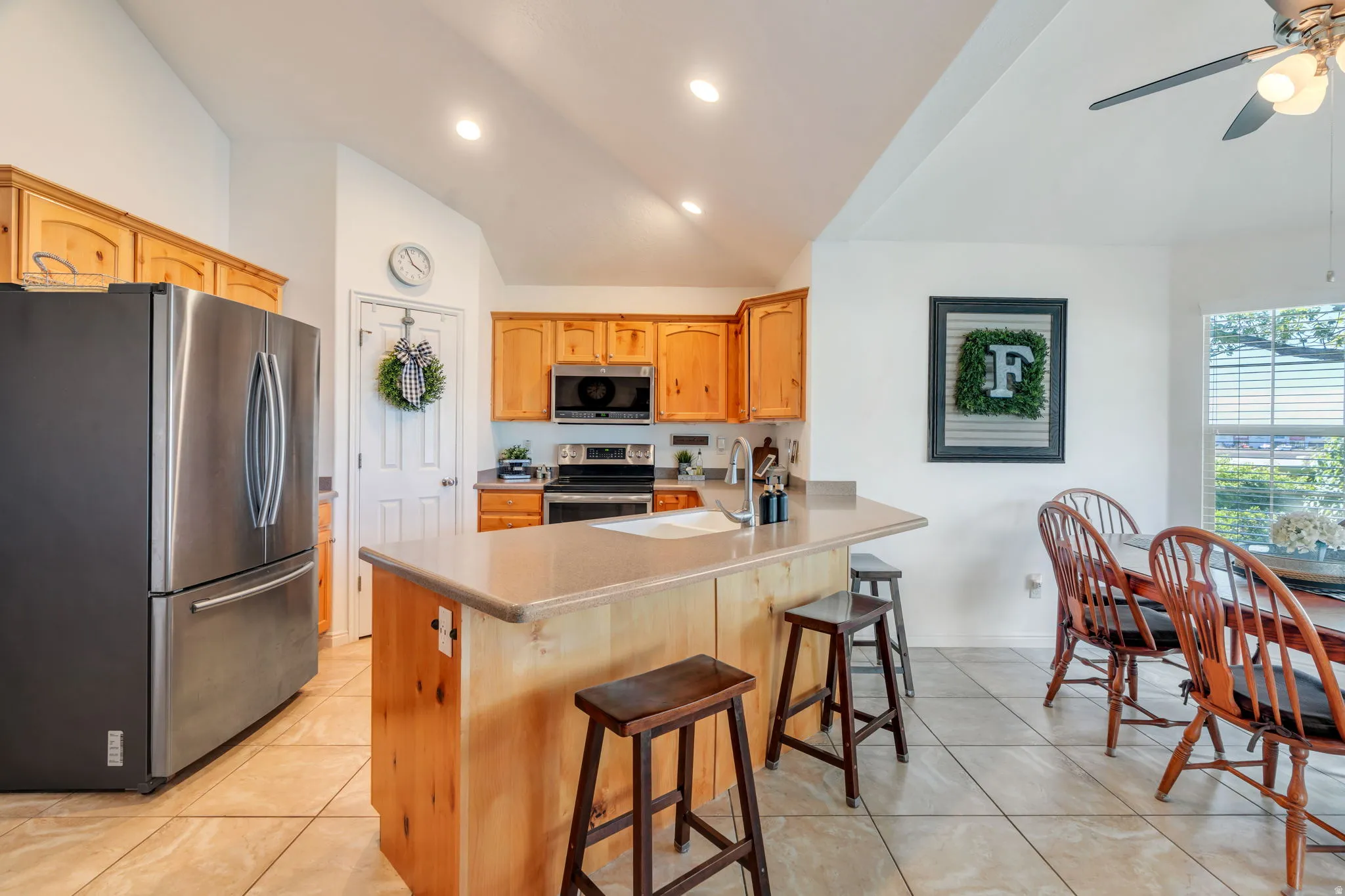 Kitchen featuring stainless steel appliances, a peninsula, lofted ceiling, a breakfast bar area, and light countertops