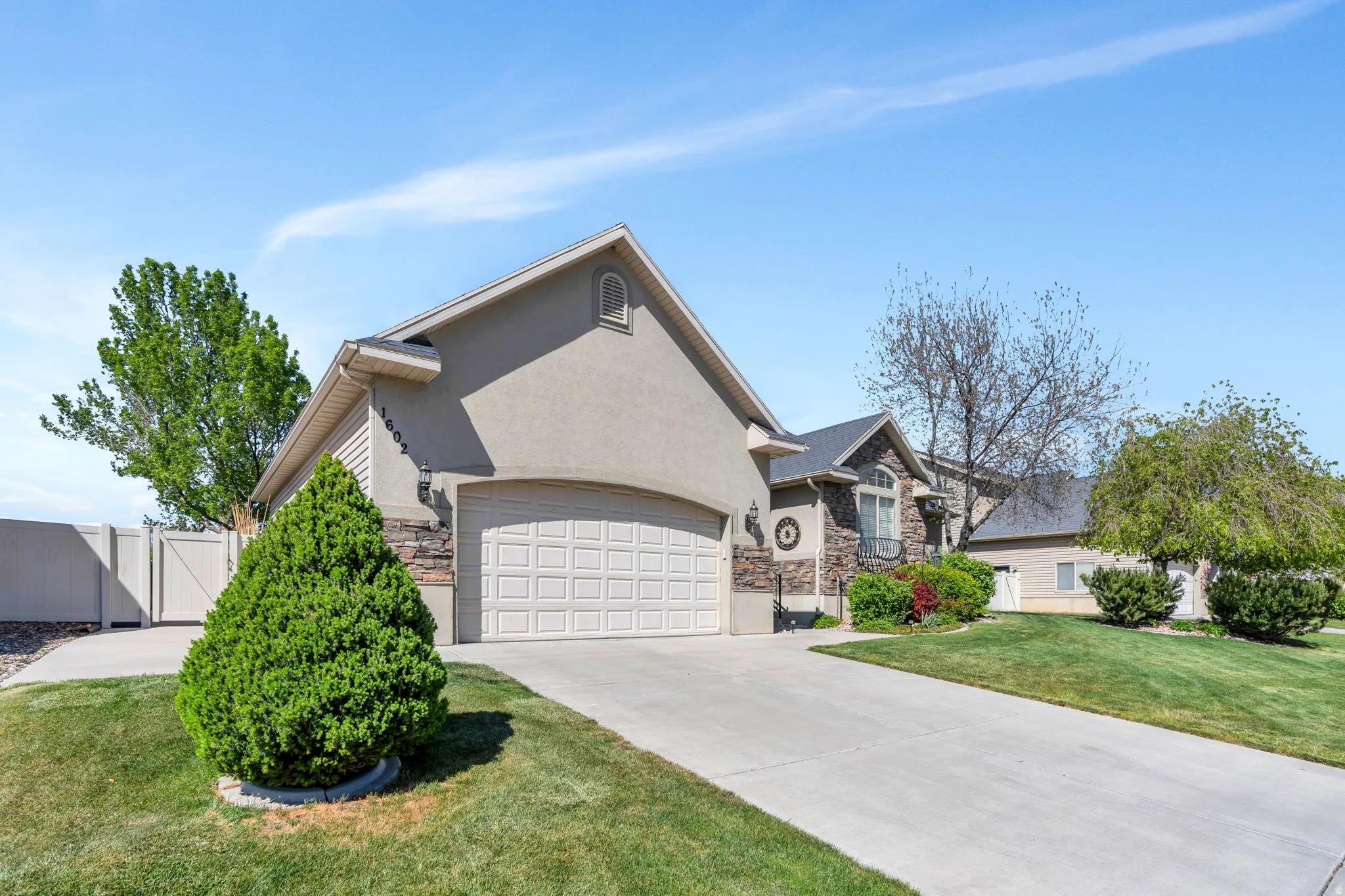 View of front of house featuring stone siding, driveway, a garage, stucco siding, and a gate