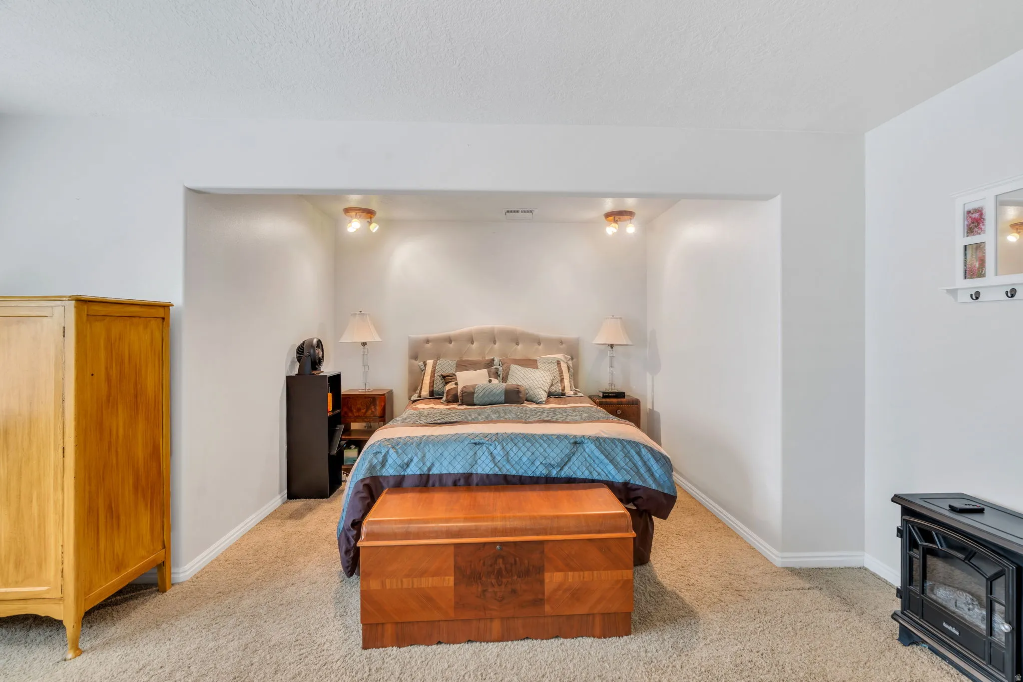Bedroom with a wood stove, light colored carpet, and a textured ceiling