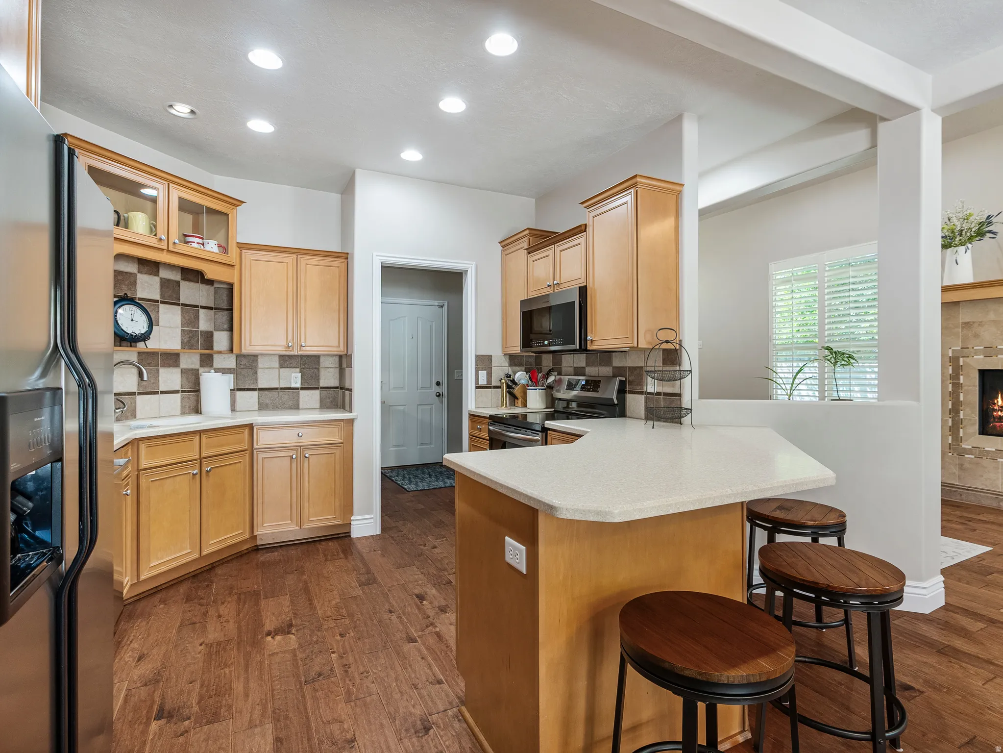 Kitchen featuring wood-finish flooring, recessed lighting, light-toned cabinetry, a built-in microwave, and a breakfast bar with a light-colored countertop