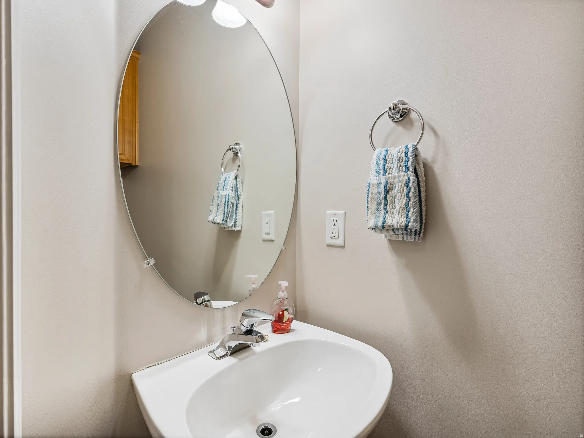 Pedestal sink with chrome faucet, complemented by an oval mirror and light beige walls