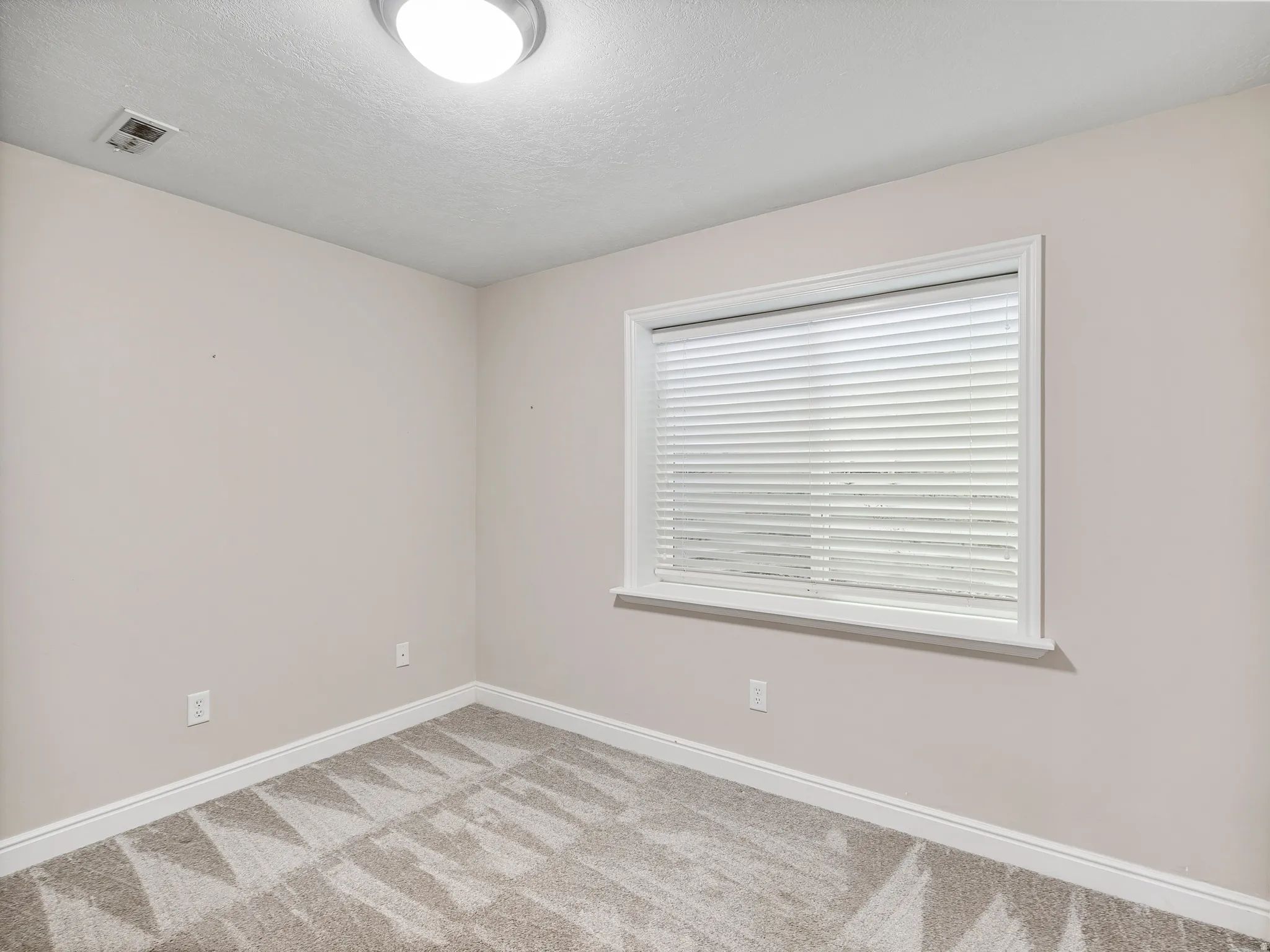 Bedroom featuring a window with horizontal blinds, neutral-toned walls, and patterned carpet flooring