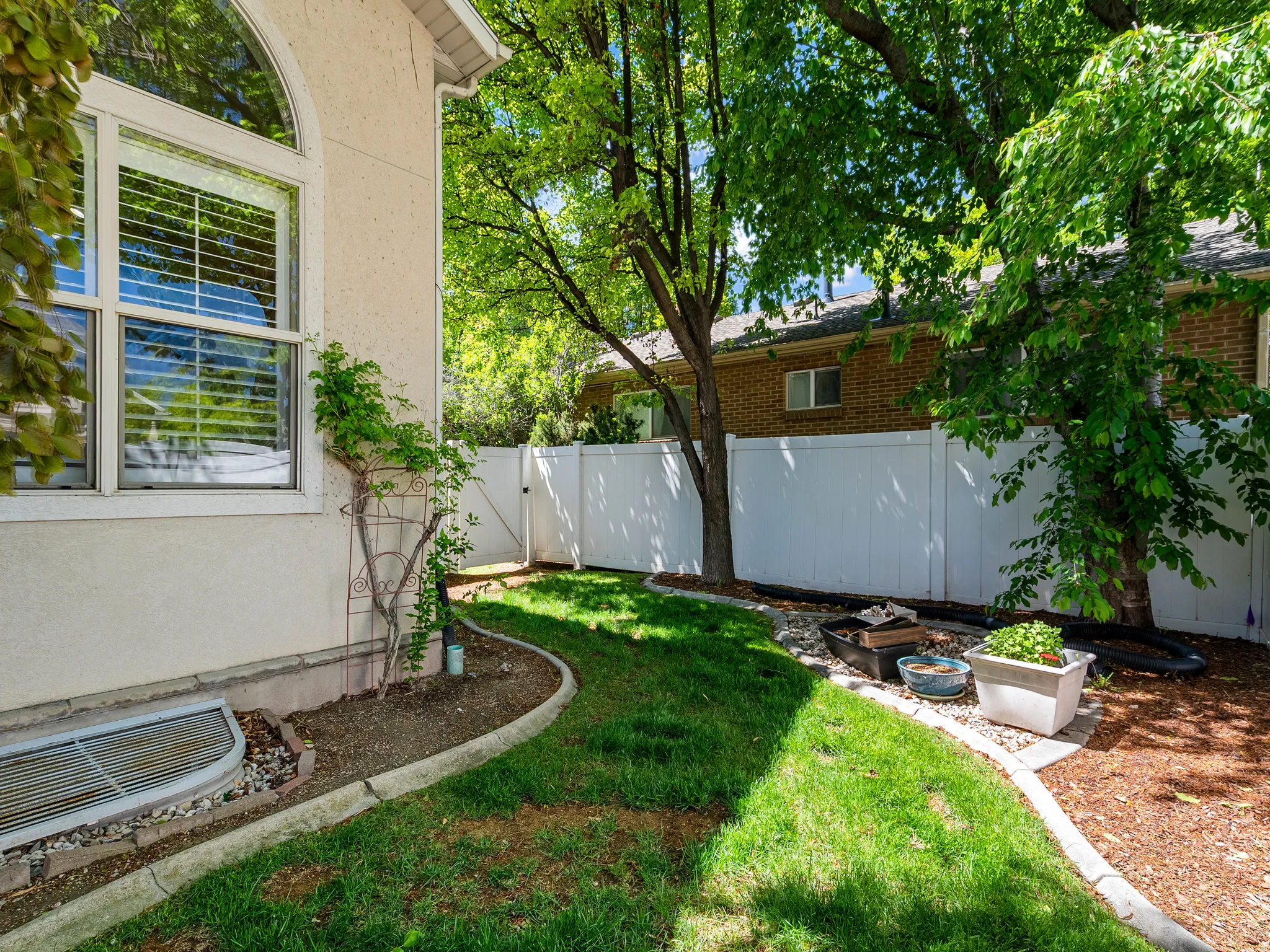 Manicured side yard featuring a white privacy fence and mature trees