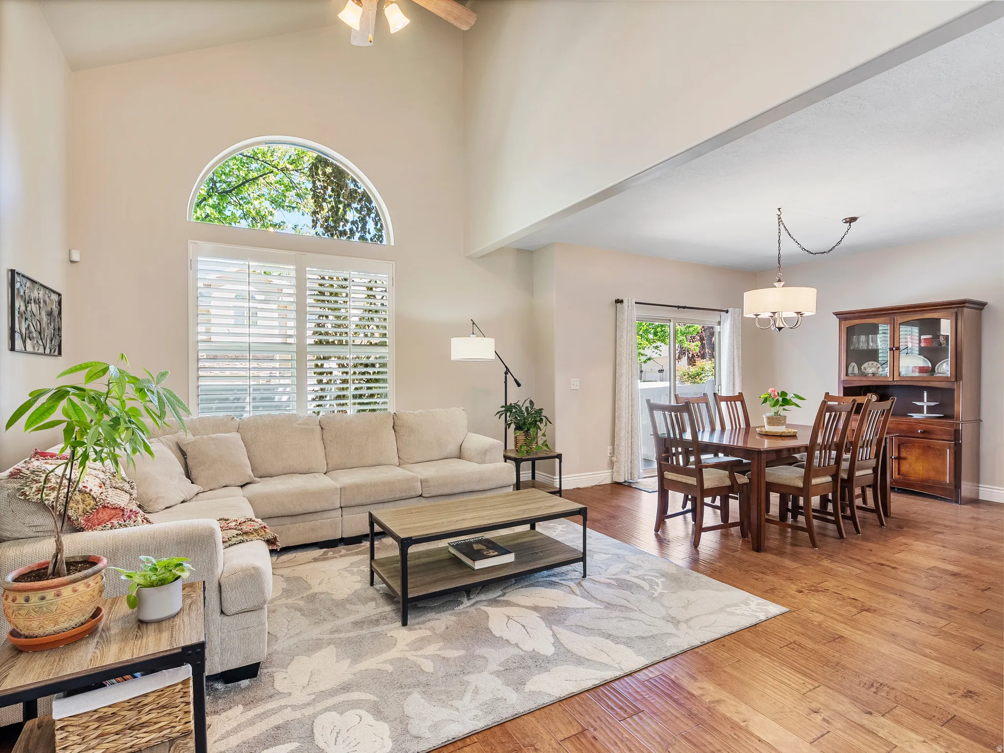 Vaulted ceilings with a ceiling fan, a large arch-top window, and plantation shutters define this living space