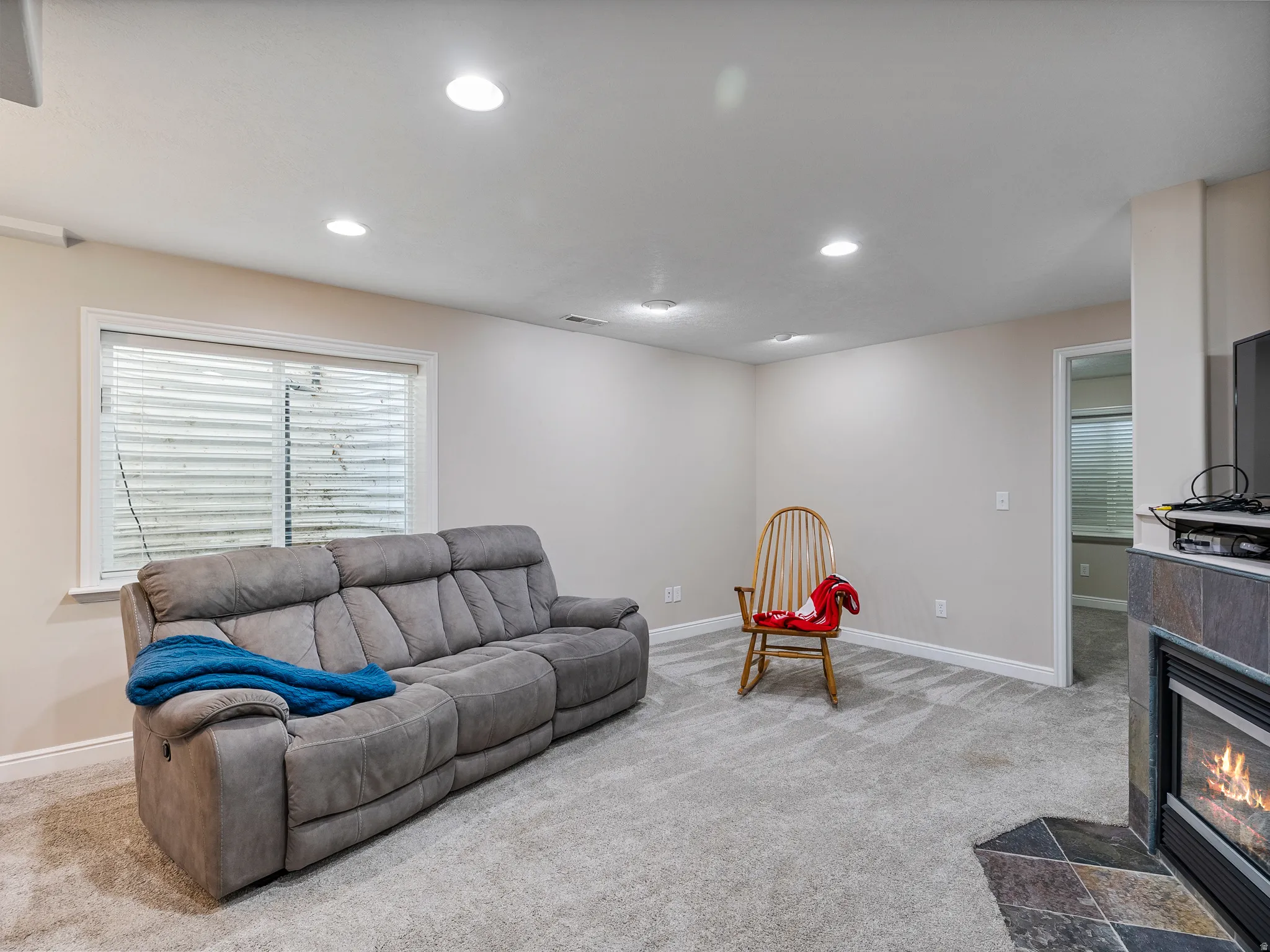 Carpeted living space featuring recessed lighting, a window with horizontal blinds, and a built-in fireplace with a stone surround and hearth