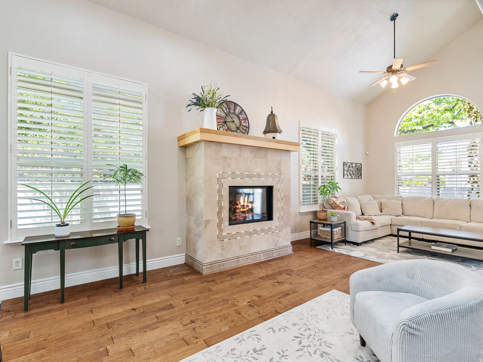 Warm living area featuring a stone-clad fireplace with an integrated firebox, vaulted ceilings, and a ceiling fan