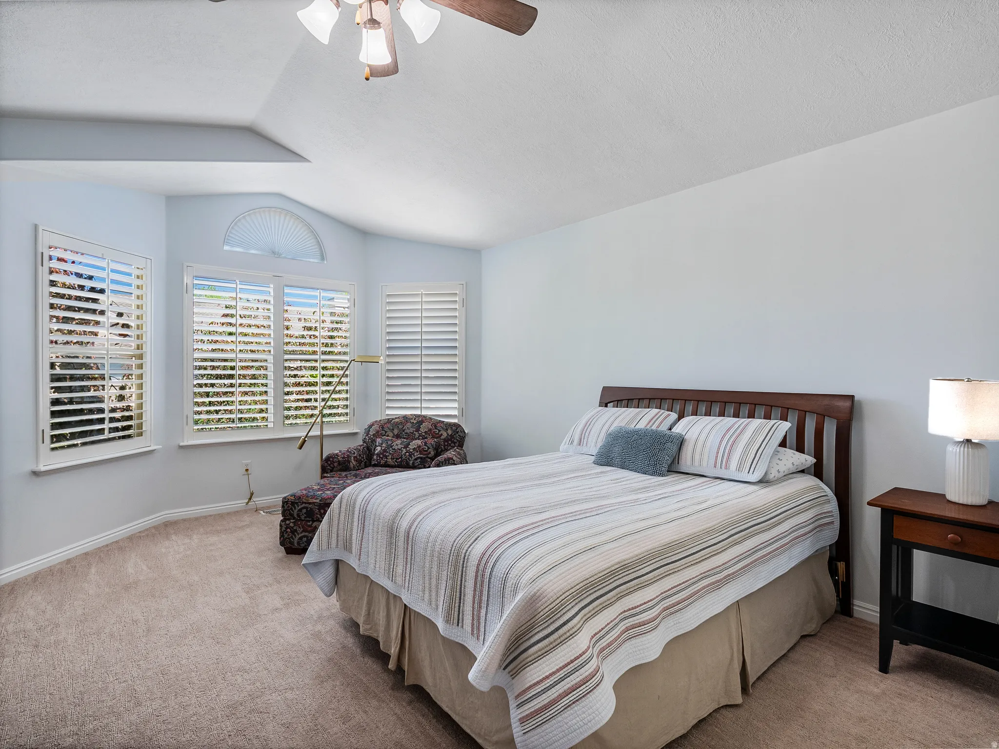 Vaulted ceiling with a ceiling fan, multiple windows with white plantation shutters, arched transom window, and neutral carpeting