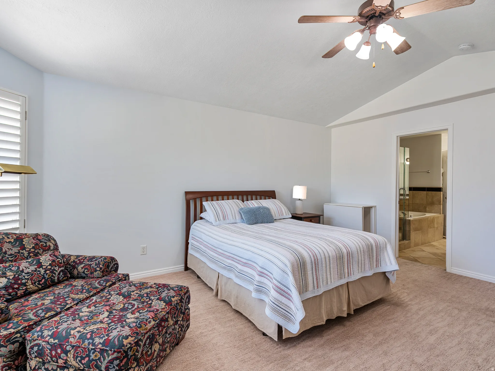 Carpeted bedroom featuring a vaulted ceiling and a ceiling fan with integrated lighting