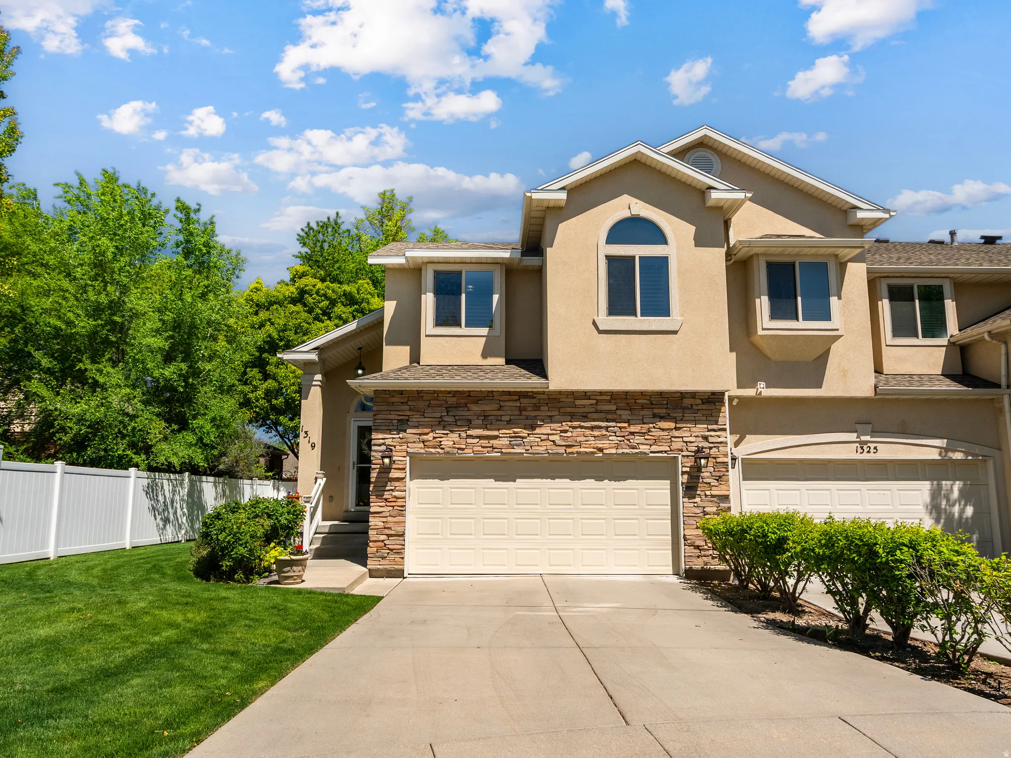 Two-story stucco exterior featuring stone accents, an arched window, a bay window, and an attached two-car garage